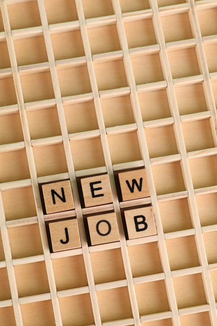 about-us-01 Overhead view of Scrabble tiles arranged to spell 'New Job' on a wooden grid background.
