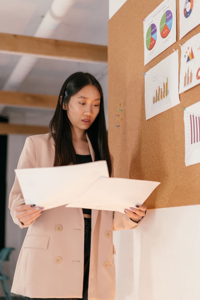 about-us-02 Asian woman in corporate attire reviewing business analytics charts on bulletin board.